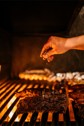 A chef's hand sprinkling salt on top of a large steak on the grill.